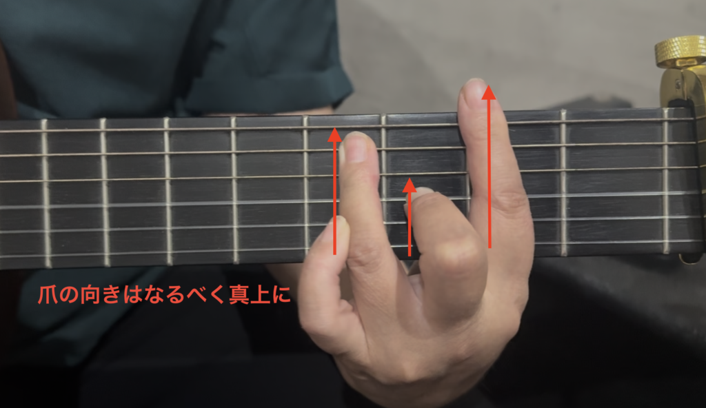 ギター講師が生徒のバレーコードを指導する様子。人差し指を少し寝かせて側面の骨を当て、爪の向きを真上にするポイントを矢印とコメントで解説した手元写真。