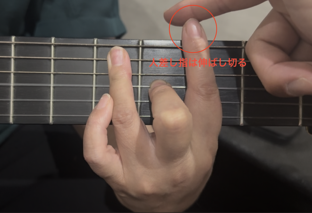 講師が生徒の人差し指を真っ直ぐ伸ばすよう調整している手元画像。第二関節が曲がらないよう、指全体で弦をしっかり押さえるポイントを強調したバレーコードのフォーム矯正写真。