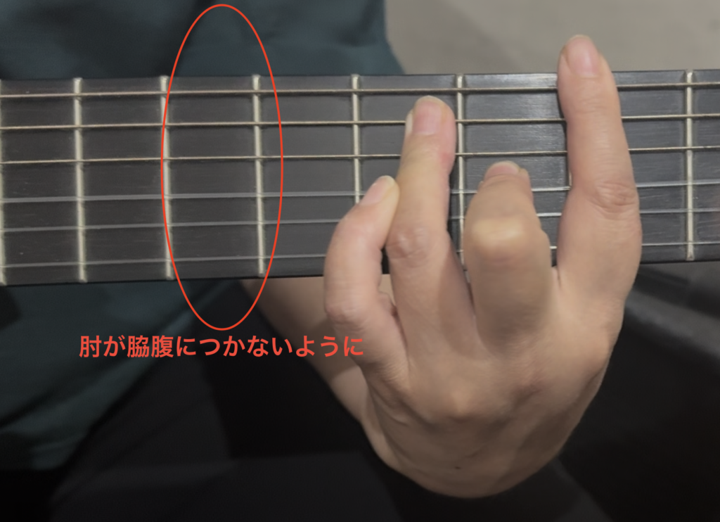 講師が生徒の肘が脇腹につかないよう指導している様子。肘を離して指の可動域を確保するコツを、矢印による視覚的なアドバイスで解説したギター教室のレッスン画像。