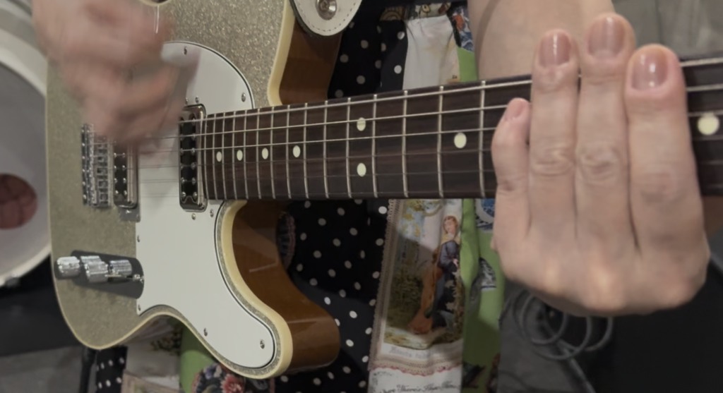 調布のギター教室でのレッスン風景。講師がストローク時に弦を押し込みすぎている手元の動きを指摘し、音がこもってしまう原因を具体的に解説している写真。