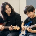 保護者が見守る中で大屋真太郎講師とギターを練習する小学生