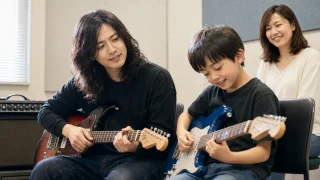 保護者が見守る中で大屋真太郎講師とギターを練習する小学生