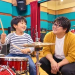 ピクミン講師と小学生が笑顔でドラムを練習し保護者が見守る様子
