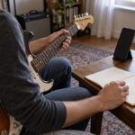 ギターとスマートフォンをそばに置き練習ノートを確認する場面