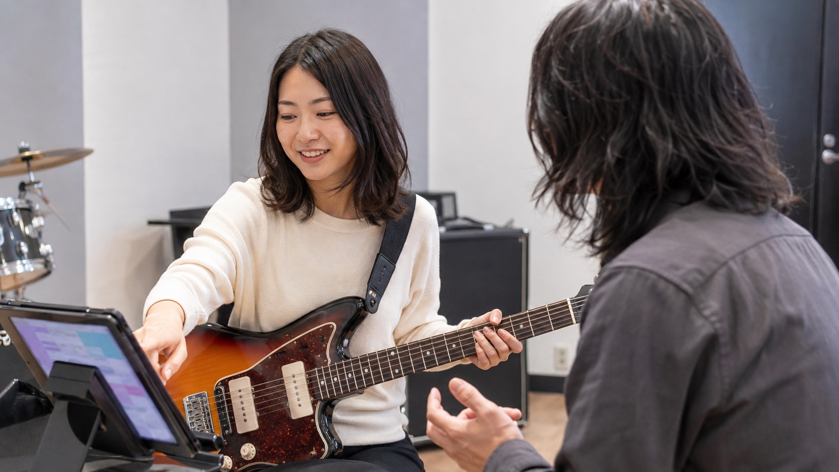 ギターを抱え、タブレットの教材を見ながら相談する女性
