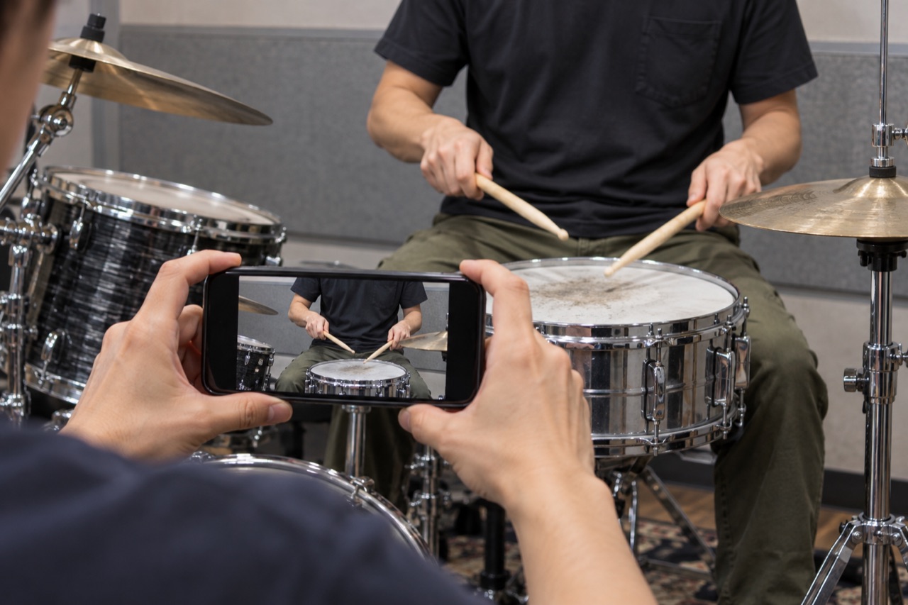 西荻窪ドラム教室：講師のドラムの手本をスマートフォンで撮影する手元（AI生成イメージ）