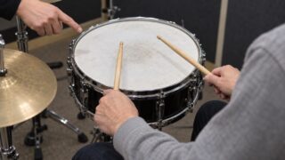 スネアの上にスティックを構えた両手と打面を示す手