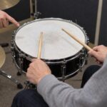 スネアの上にスティックを構えた両手と打面を示す手